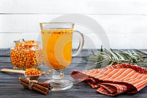 Colorful hot natural sea buckthorn tea in a glass cup, fresh raw berries  and cinnamon sticks. Vitaminic healthy medicine drink.