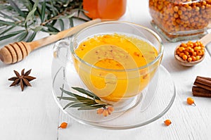 Colorful hot natural sea buckthorn tea in a glass cup, fresh raw berries and leaves, honey, anise and cinnamon sticks. Vitaminic