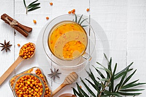 Colorful hot natural sea buckthorn tea in a glass cup, fresh raw berries and leaves, honey, anise and cinnamon sticks. Vitaminic