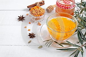 Colorful hot natural sea buckthorn tea in a glass cup, fresh raw berries and leaves, honey, anise and cinnamon sticks. Vitaminic