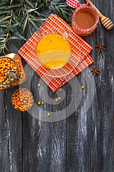 Colorful hot natural sea buckthorn tea in a glass cup, fresh raw berries and leaves, honey, anise and cinnamon sticks. Vitaminic