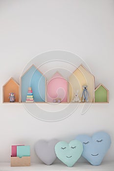 Colorful house shaped shelves on white wall and soft pillows. Children`s room interior design