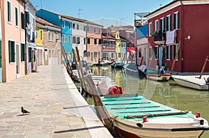 Colorful houses along the canal with parked boats on Burano island, Venice, Italy. Attractive famous travel destination