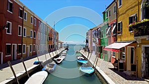 Colorful houses and boats moored along canal on Burano island, locals in street photo