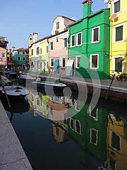 Colorful houses and boats with reflections in the canal on the island of Burano in Venice