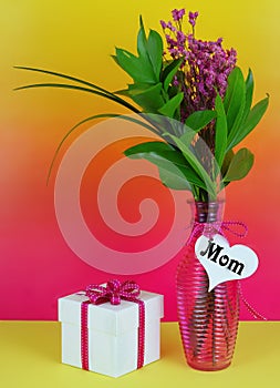 Colorful image of pink dried flowers with large green leaves in a ribbed pink vase for mother`s day