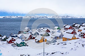 Colorful inuit houses among rocks and snow at the fjord in a sub