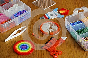 Colorful iron beads in a box, art toys created from them and white tweezers on wooden background