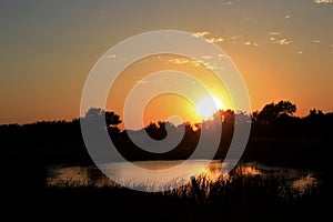 Colorful Kansas sky with clouds and a reflection on a farm pond and tree silhouettes that`s bright and colorful out in the country