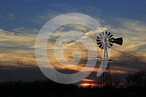 Colorful Kansas Sunset with clouds, tree`s and a Windmill silhouette out in the country.