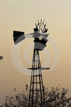 Colorful Kansas Sunset with a Smokey sky Windmill silhouette and a tree.