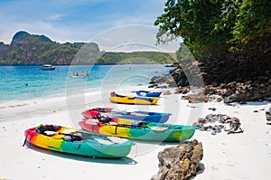 Colorful kayaks on the beach with tourist behind and the boats