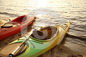 Colorful kayaks with paddles near water on river beach at sunset. Summer camp activity