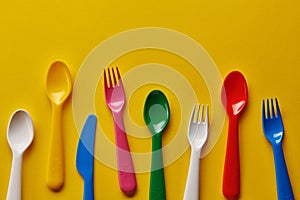 Colorful kids plastic spoons on yellow background. Many, utensils.