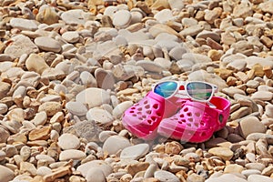 Colorful kids sandals on a pebble beach. kid`s summer plastic shoes and summer sunglasses on the rocky beach. Copy space