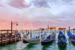 Colorful landscape with sunset sky, rainbow and gondolas parked near piazza San Marco in Venice. Church of San Giorgio Maggiore on