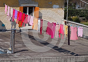 Colorful laundry hanging to dry on a clothesline in a terrace.  The clothes colors are mostly pink purple and red