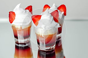 Colorful layered shots of drinks based on vodka, grenadine and orange juice decorated with whipped cream and pieces of strawberry