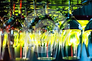 Colorful lights of the bar are reflected in clean empty glasses above the bar counter. Interior of pub or bar at night