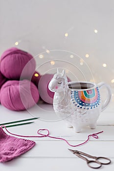 Colorful Llama shaped tea or coffee mug with knitting needles, scissors and wool yarn, garland background