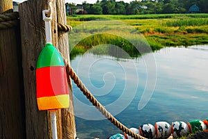 A colorful lobster buoy hangs on a post near a salt marsh