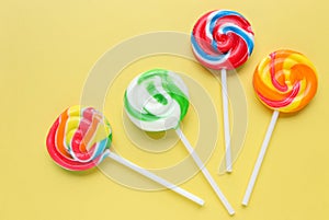 Colorful lollipops, different colored round candy on sticks on yellow background.