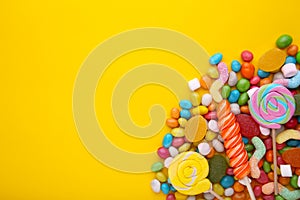 Colorful lollipops and different colored round candy on yellow background