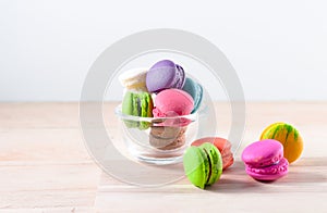 colorful macarons in transparent cup on table over wooden background
