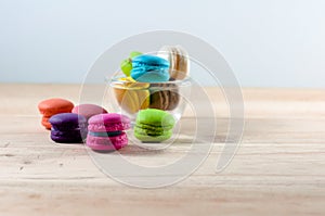 colorful macarons in transparent cup on table over wooden background