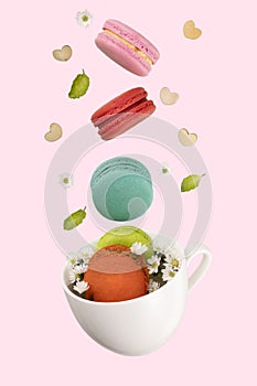 Colorful macarons, white little flowers, green mint leaf, amd wooden hearts floating on a white tea cup