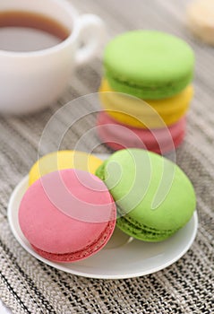 Colorful macarons on white plate and cup of tea