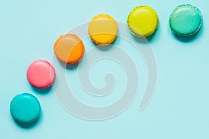 Colorful macaroons arranged like rainbow over blue background.