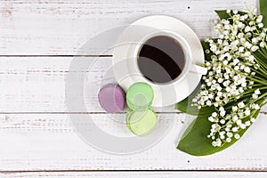 Colorful macaroons, a cup of coffee and lilies of the valley on wooden background, close-up flat lay