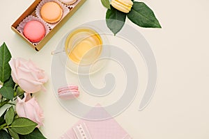 Colorful macaroons and rose flowers with tea on light green. Sweet macarons in gift box. Top view