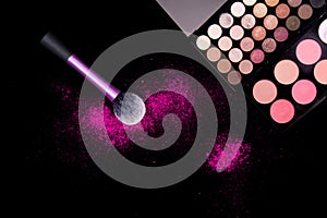 Colorful makeup palette and pink big brush to apply powder on pure black background. Professional makeup equipment.