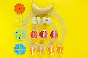 Colorful math fractions and apples, oranges, banana as a sample on yellow background or table. Interesting fun math for kids.