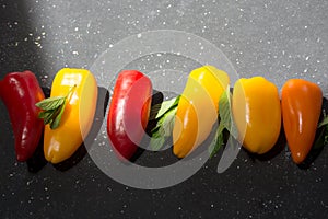 colorful mini peppers and mint leaves on black sunny background. Above view of yellow, red and orange peppers