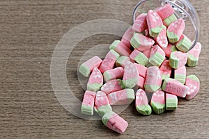 Colorful miniature marshmallows in a glass spilled on a wooden background