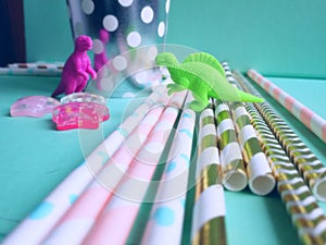 Colorful mint, pink and golden drinking straws for beverages with dinosaur toys. Party theme composition