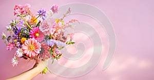 Colorful Mixed Bouquet Held in Hand Against Pink Background. Flower present. Summer garden bouquet