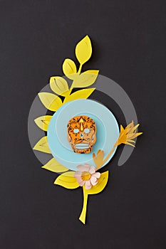 Colorful modern Calaca composition from paper with yellow leaf and decorative skull on a black paper background.