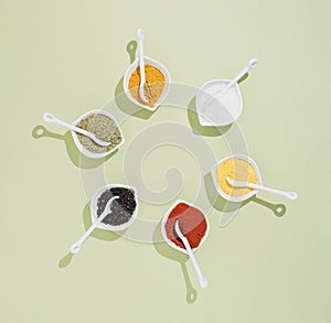 Colorful and modern layout made with kitchen spices in small white bowls, with white spoons, on pastel green background. Flat lay