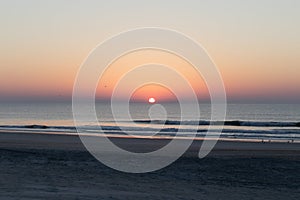 Colorful morning sun ascending over the ocean, deserted beach with calm waters