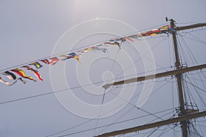 Colorful nautical sailing flags flying in the wind from the lines of a sailboat mast backlit in bright blue sky by the