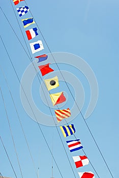 Colorful nautical sailing flags flying in the wind from the lines of a sailboat mast backlit in bright blue sky by the sun