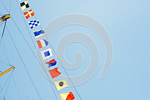 Colorful nautical sailing flags flying in the wind from the lines of a sailboat mast backlit in bright blue sky by the sun