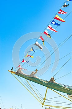 Colorful nautical sailing flags flying in the wind from the lines of a sailboat mast backlit in bright blue sky by the sun