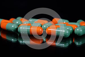 Colorful oblong pharmaceutical capsules on reflective surface, black background