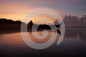 Colorful orange blue sky over the sea at sunrise. Morning sky with clouds, smooth waves and traditional fishing boat silhouette.