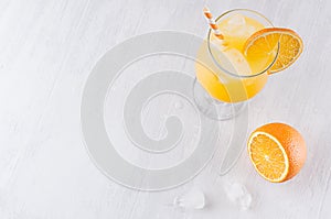 Colorful orange cool citrus cocktail with slice oranges, ice cube, straw on white modern wooden background, top view.